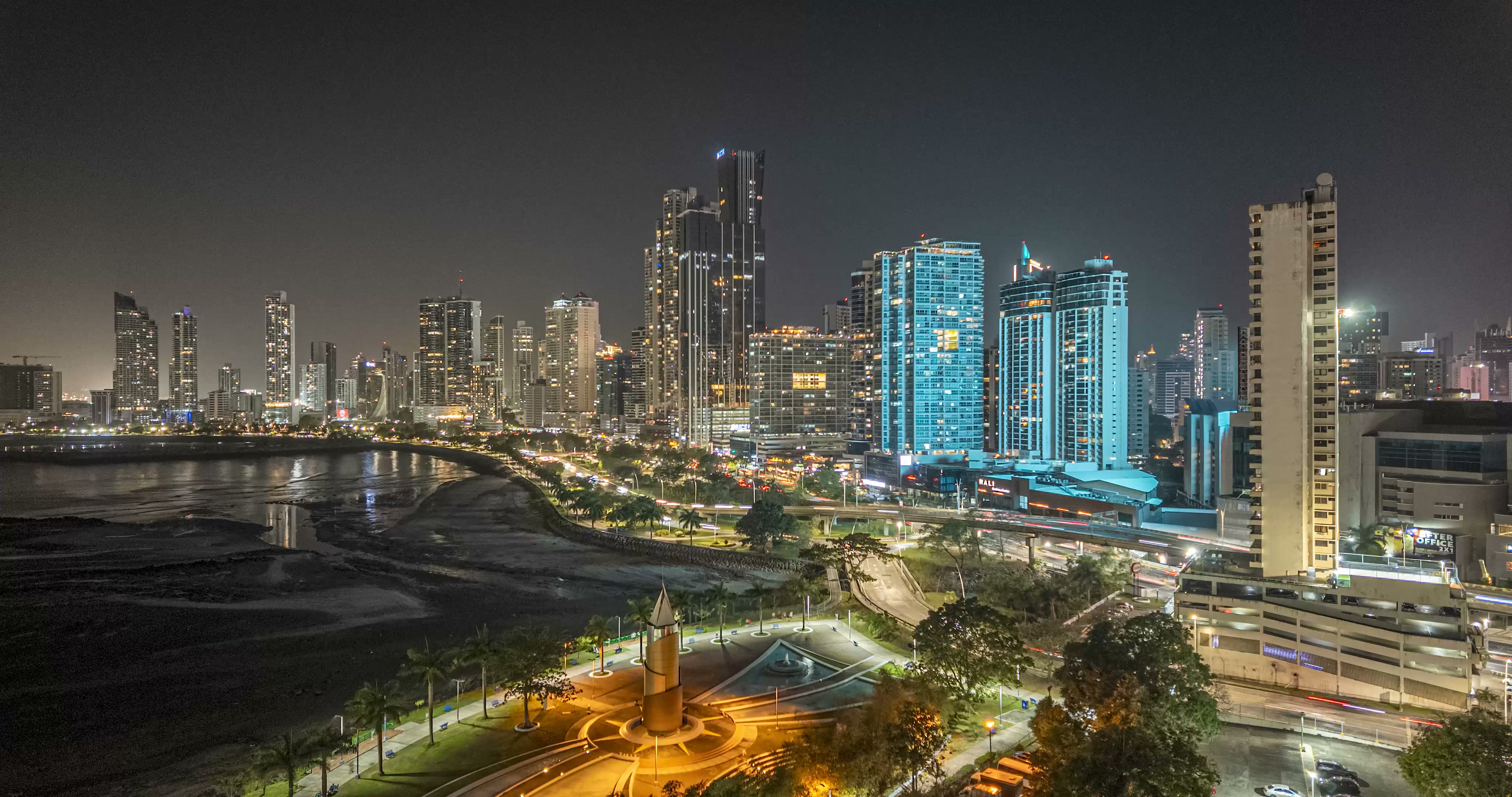 Nighttime coastal skyline with blue-lit towers reflected in the water